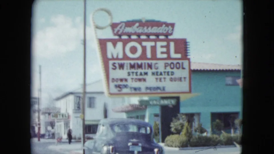 1959 Nevada street-side view of an Ambassador Motel sign with a parked car and low motel building.