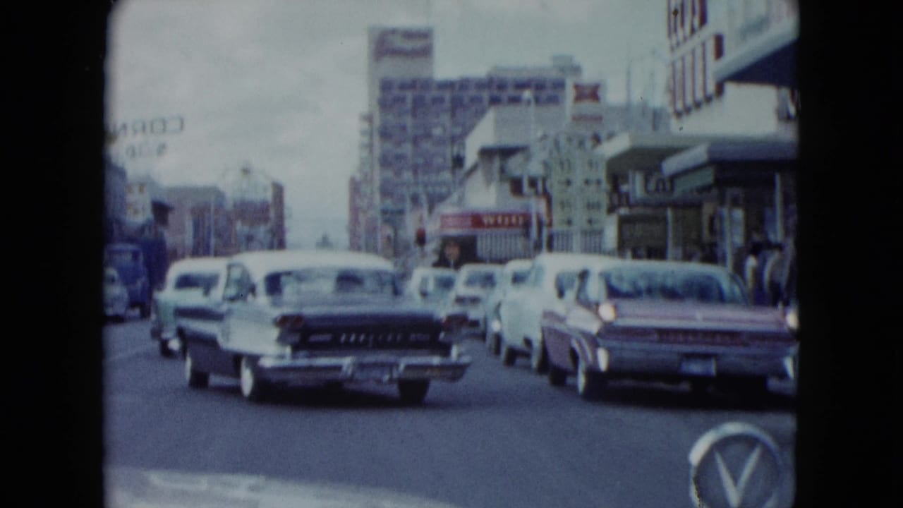 1959 Nevada street view from moving traffic with classic cars, storefronts, and distant neon signage.