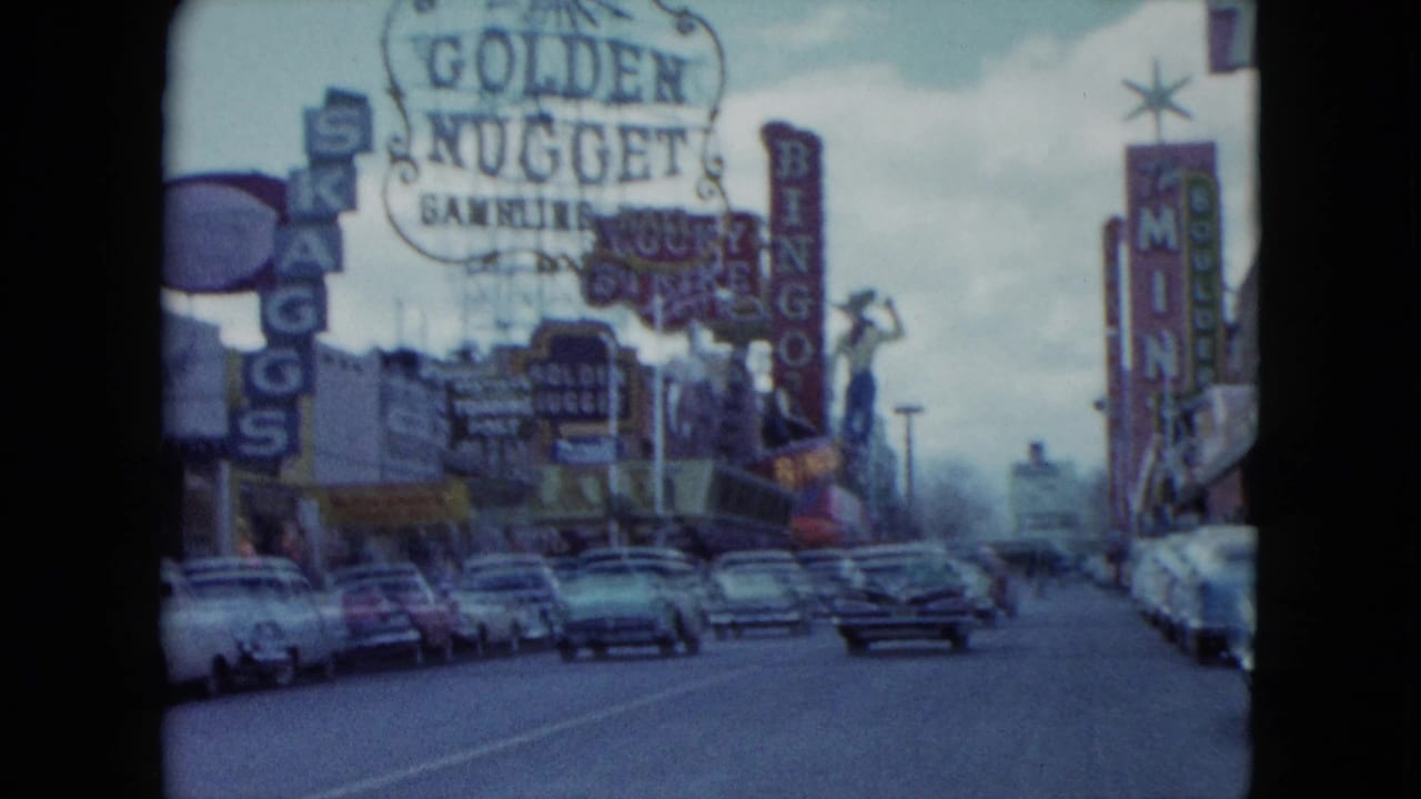 Casino signs and parked cars line a broad street with traffic ahead.