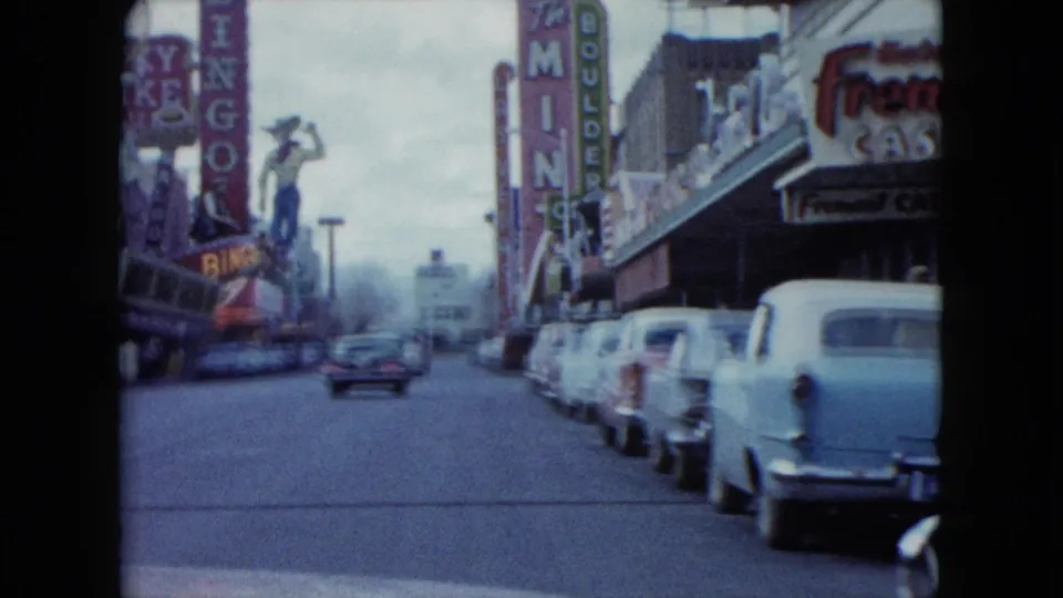 1959 Nevada 8mm driving view with a cowboy figure sign, casino marquees, parked cars, and storefronts.