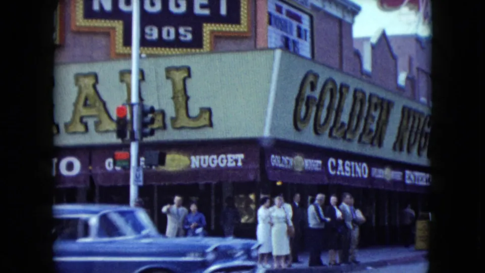 1959 Nevada home-movie frame showing the Golden Nugget facade, pedestrians on the sidewalk, cars, and a traffic light.