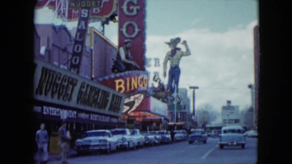 1959 Nevada street view looking past Golden Nugget signage toward vintage traffic and a large western figure above the casino frontage.