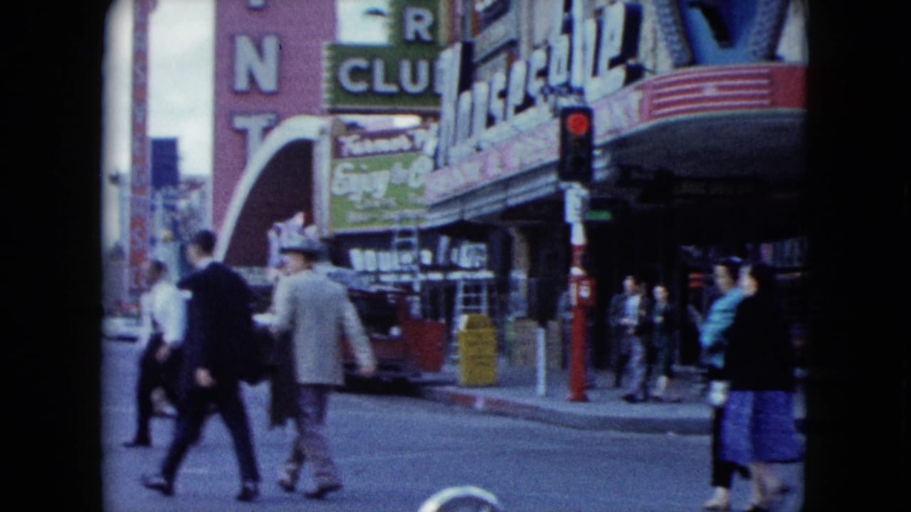 1959 Nevada street view with pedestrians crossing beneath casino-front signage and a red traffic signal.