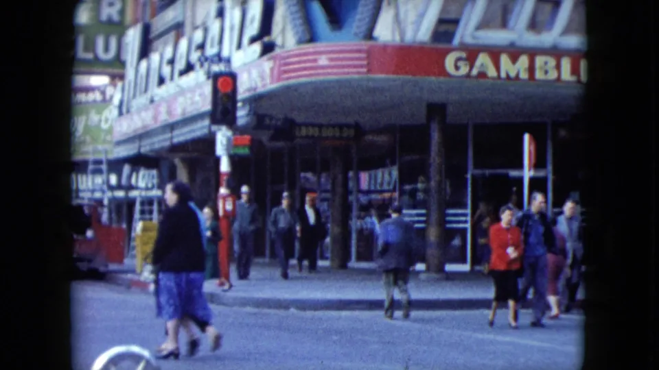 1959 Nevada sidewalk scene with pedestrians near the Gambler sign, storefront doors, and a red signal.