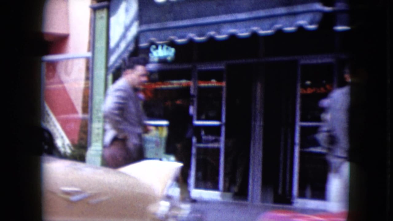 1959 Nevada street view with a suited pedestrian, glass storefronts, awning, and a classic car moving through the foreground.