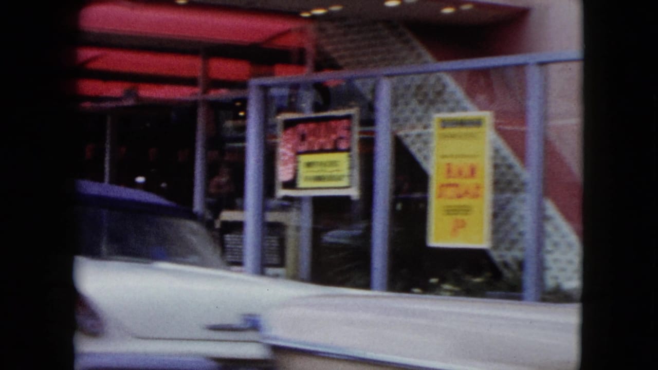 White classic car passing storefront windows beneath a red awning.