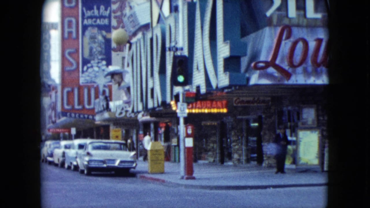 1959 Nevada street view with parked mid-century cars, large casino and arcade signage, storefronts, and a green traffic signal.