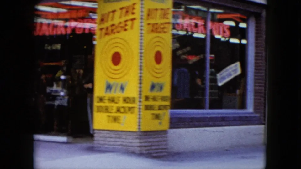 1959 Nevada storefront detail with neon lettering, a large yellow Hit the Target sign, sidewalk frontage, and people near the entrance.