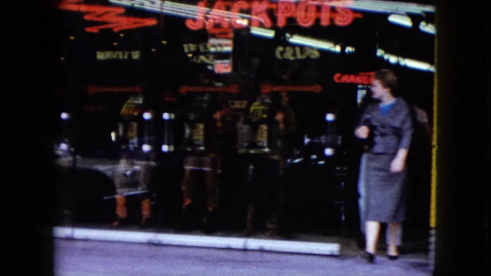 1959 Nevada sidewalk view of a woman outside a neon-lit casino or arcade storefront with reflective glass and signage.