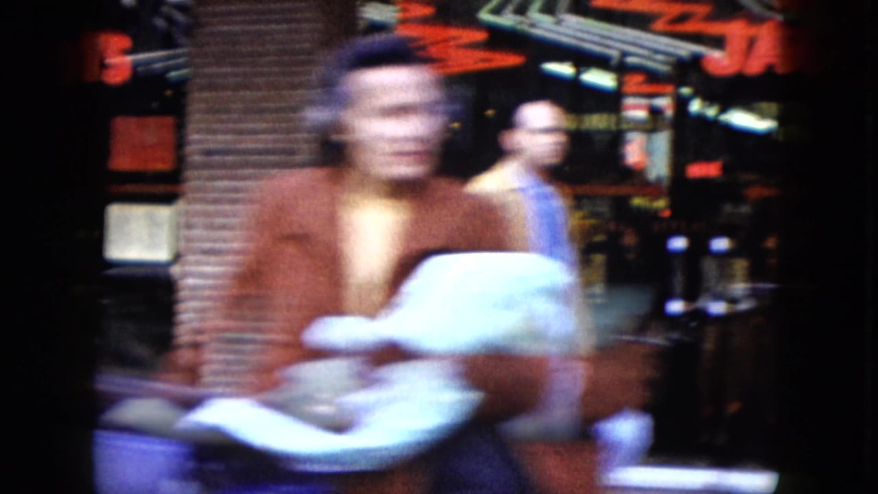 Blurred pedestrian passes neon-lit storefronts during a 1959 Nevada nighttime street view from a moving car.
