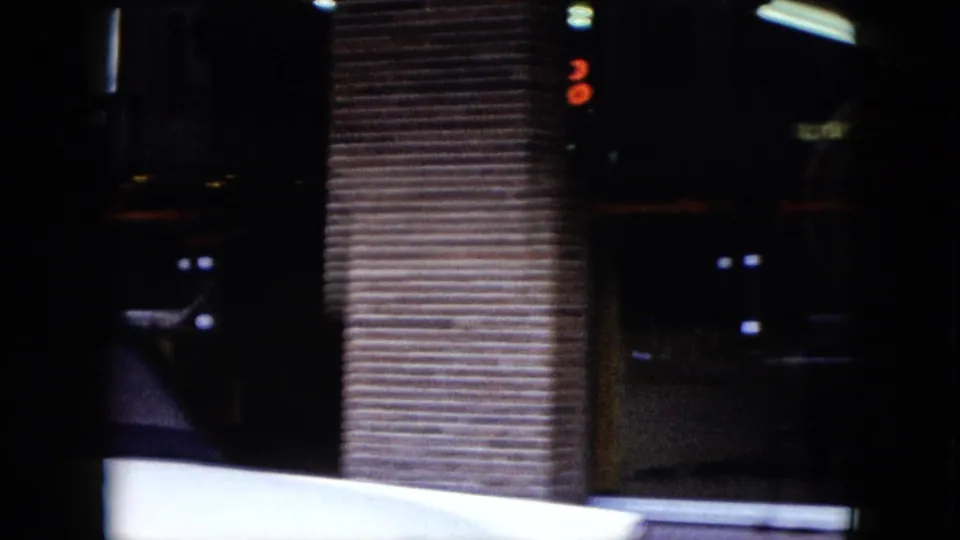 The moving 8mm view passes a dark storefront entrance, brick column, and the lower edge of a white car in Nevada.