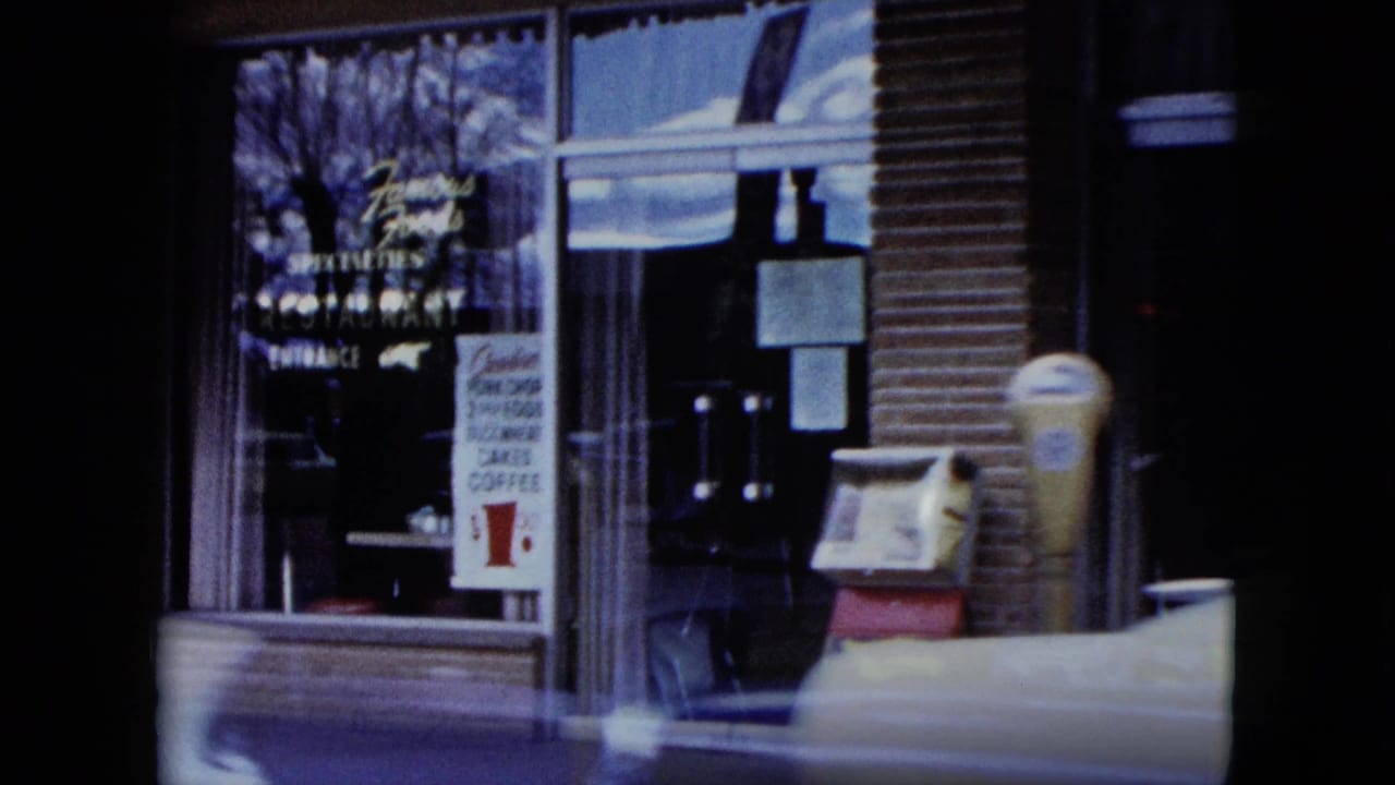 Storefront window with signs, a parking meter, and a newspaper box near the curb.