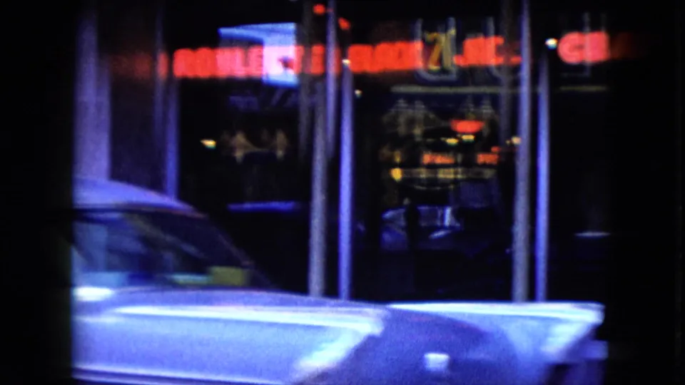 1959 Nevada street view with neon keno and jackpot signs, storefront glass, and a white car passing through the foreground.