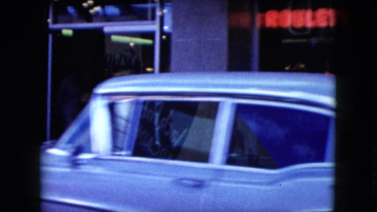 1959 Nevada home-movie frame of a light-colored station wagon moving past dark storefront windows and glowing signs at night.