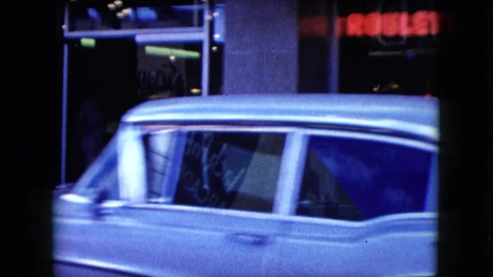 1959 Nevada home-movie frame of a light-colored station wagon moving past dark storefront windows and glowing signs at night.