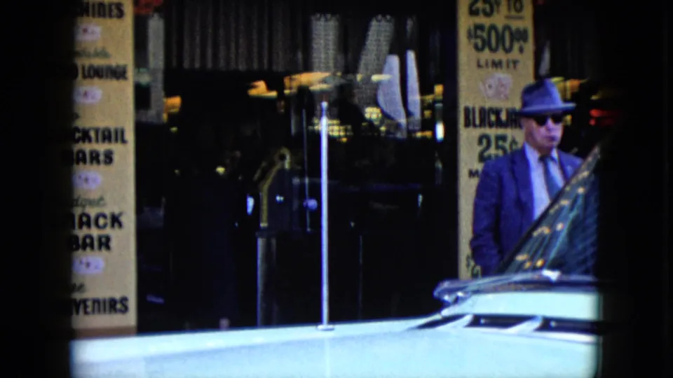 1959 Nevada sidewalk scene with a suited man in a hat near storefront bar signage, dark glass, and the front of a classic car.