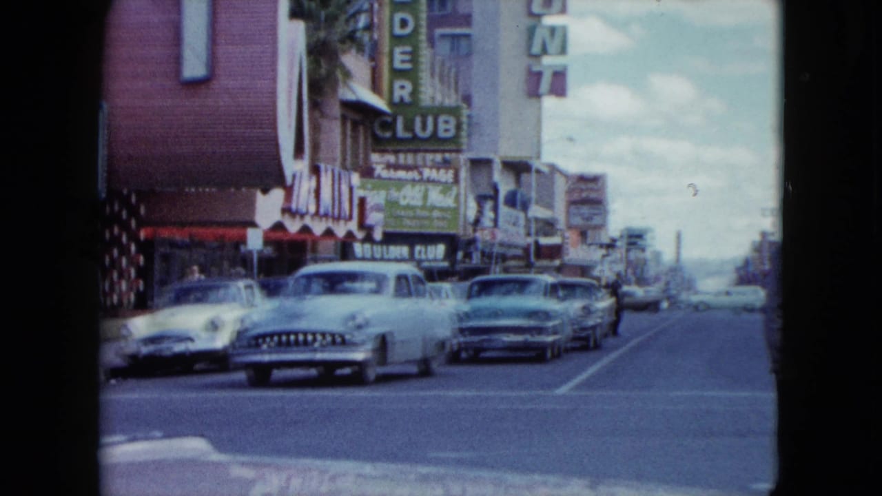 Classic cars drive past storefronts with Boulder Club and Bird Cage signs.