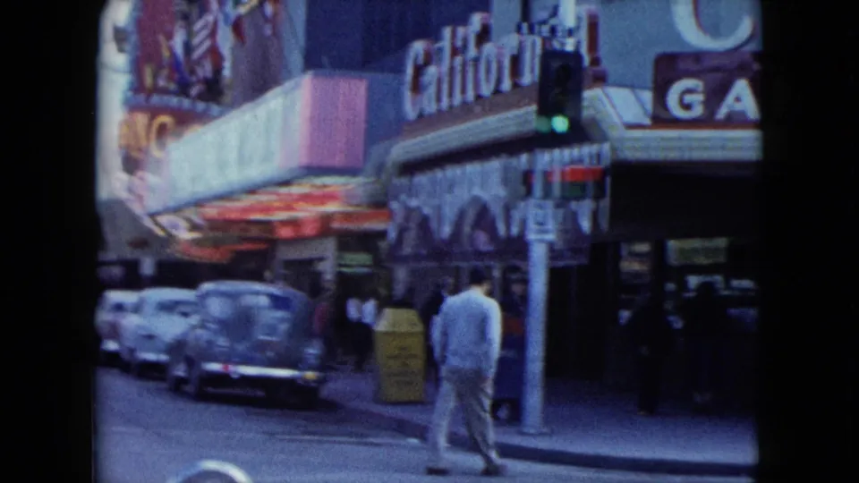 A supplied 1959 Nevada street corner shows a man walking below California Game lettering, a traffic signal, and rows of parked 1950s cars.