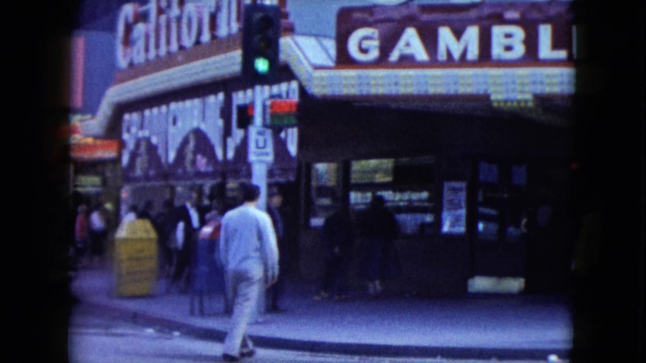 1959 Nevada street view with a man walking past a neon-lit gambling hall, pedestrians, storefronts, and a traffic signal.
