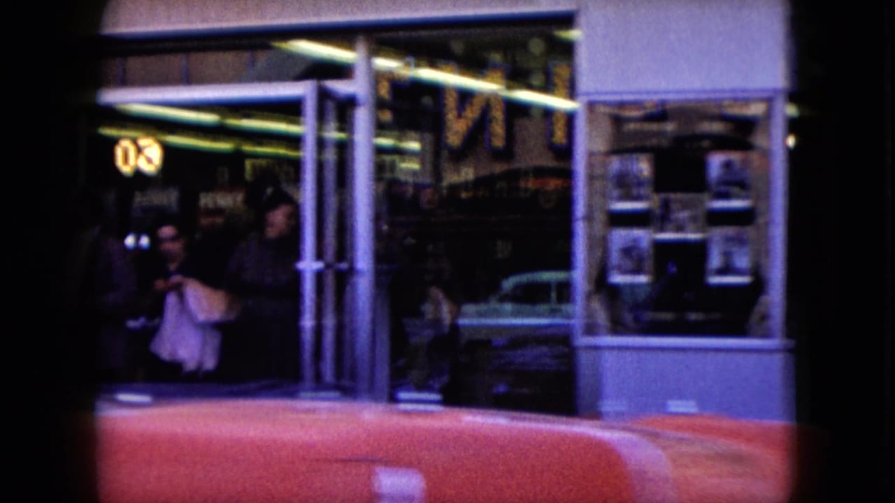 Nevada sidewalk view with pedestrians by glass storefront windows, reflected cars, neon numbers, and a red car crossing the foreground.