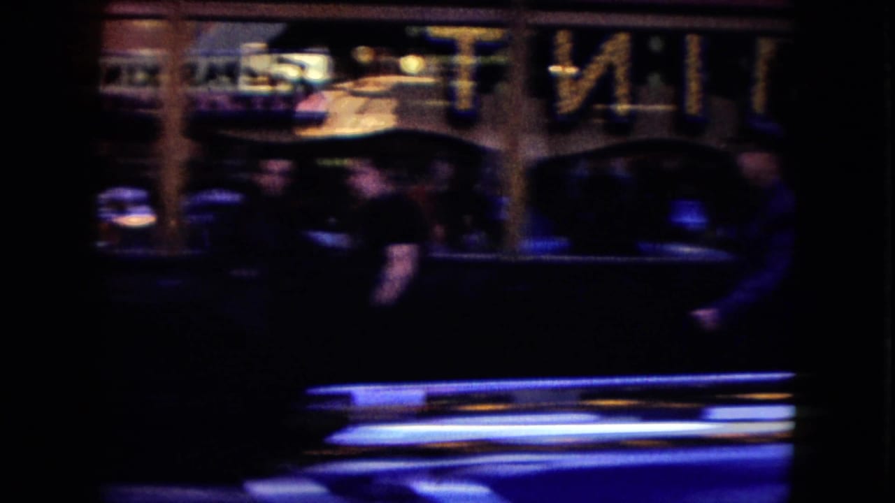 A dark mid-century car moves through a blurred Nevada street view with shopfront lighting behind it.