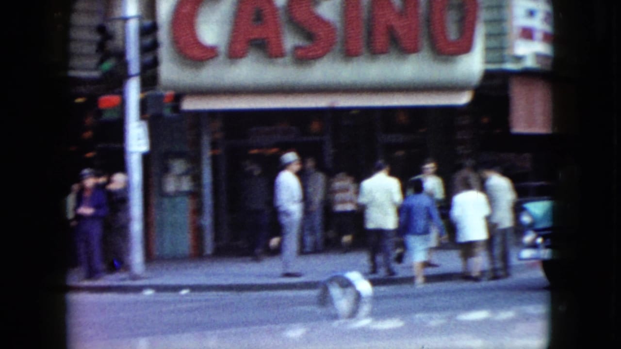 A Nevada sidewalk scene shows adults near a large casino awning and storefronts in 1959 home-movie footage.