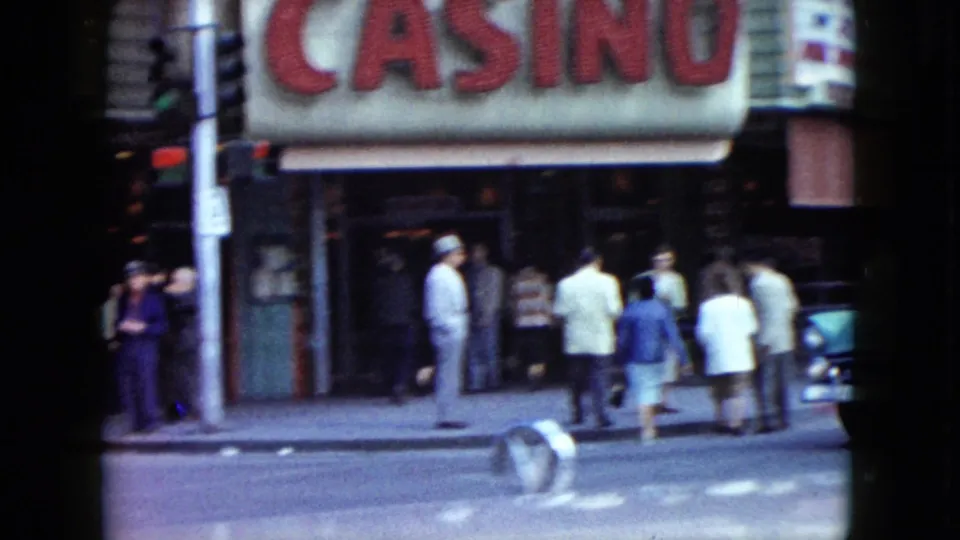 A Nevada sidewalk scene shows adults near a large casino awning and storefronts in 1959 home-movie footage.