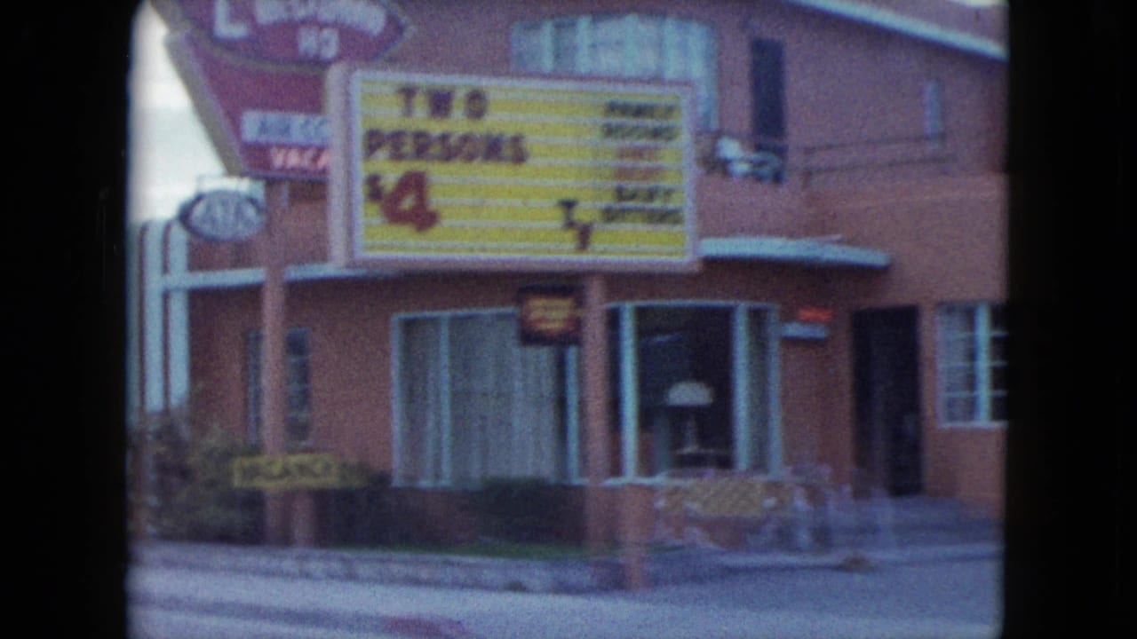 Closer view of a motel building with a large roadside sign advertising room rates.