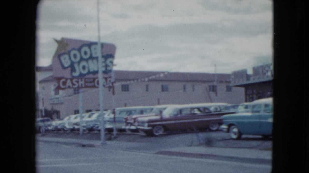 1959 Nevada street view with a large roadside business sign, parked classic cars, low-rise buildings, and traffic passing in front.