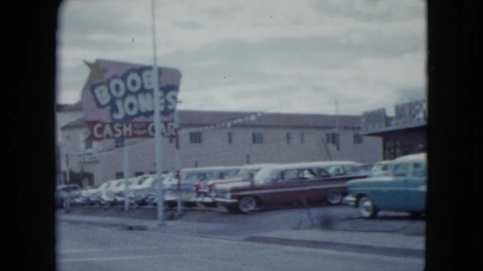 1959 Nevada street view with a large roadside business sign, parked classic cars, low-rise buildings, and traffic passing in front.