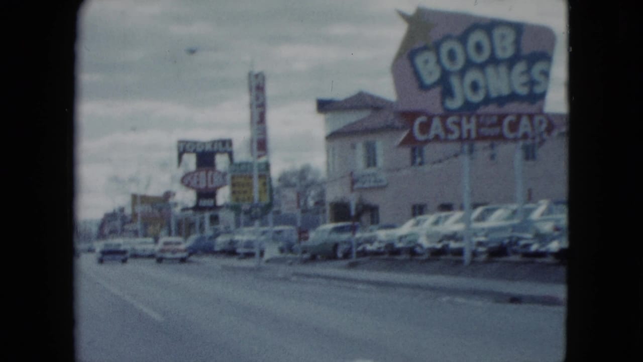 Wide 1959 Nevada 8mm street view showing roadside business signs, motel signage, rows of classic cars, and an overcast roadway.