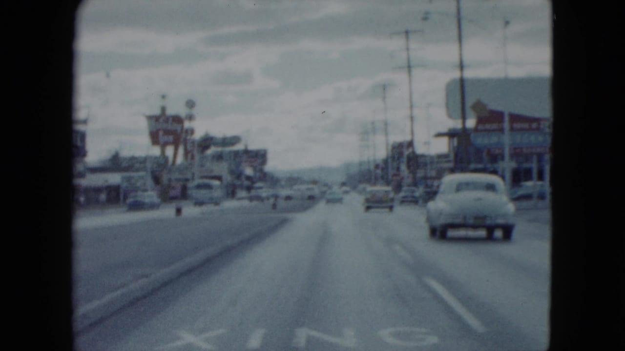 Moving 8mm street view in Nevada, 1959, showing classic cars, a raised roadside sign, utility poles, and a wide divided roadway.