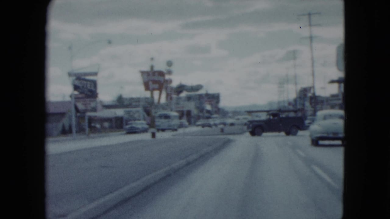 1959 Nevada home-movie frame showing a motel sign, traffic, utility poles, and a broad commercial roadway from a moving car.