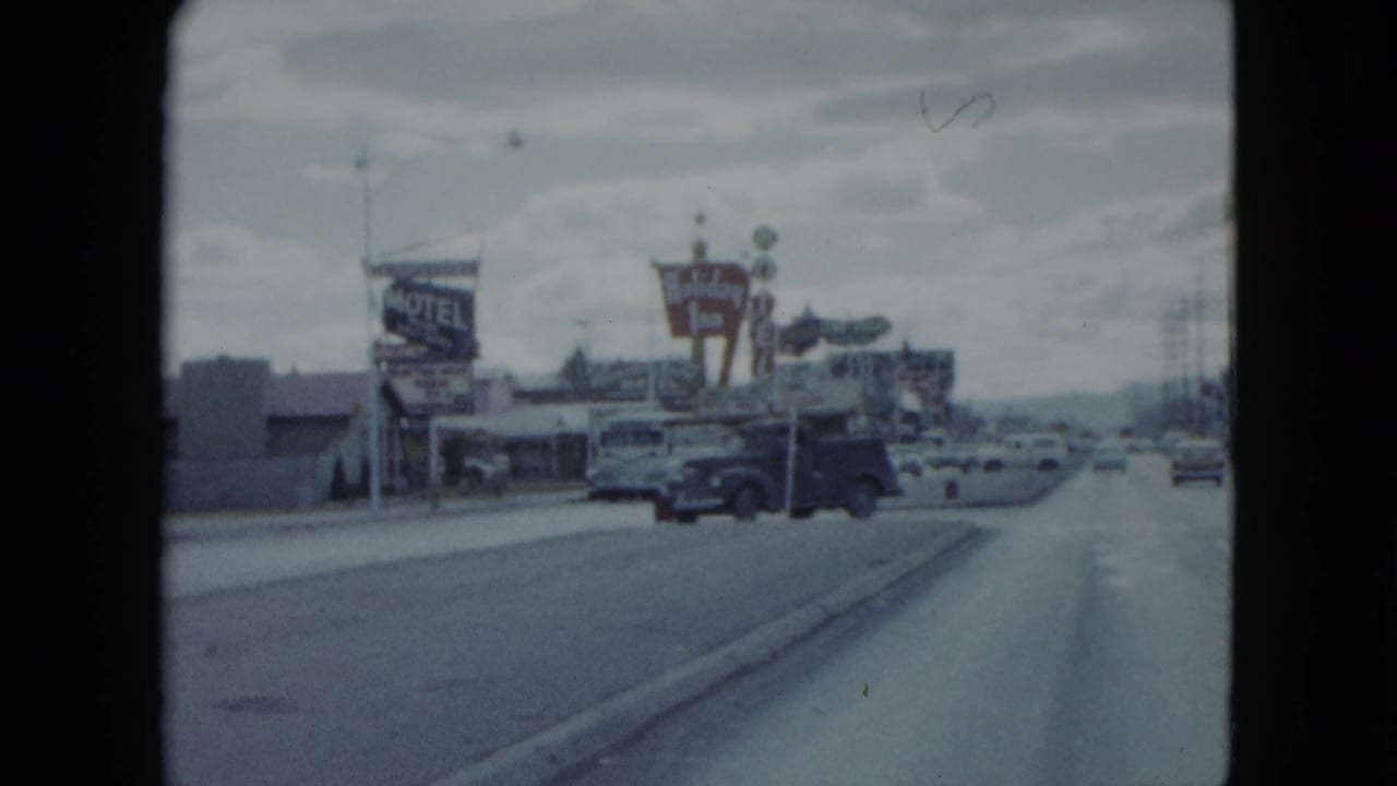 End frame of a 1959 Nevada drive showing a motel sign, parked vehicles, roadside businesses, and the divided street ahead.