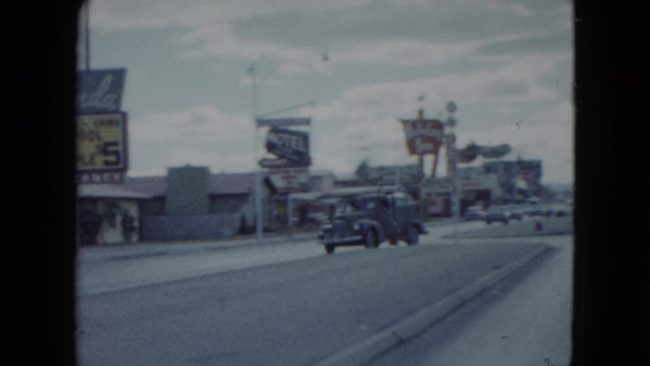 1959 Nevada home-movie frame looking down a road past vintage cars, low motel buildings, and roadside lodging signs.