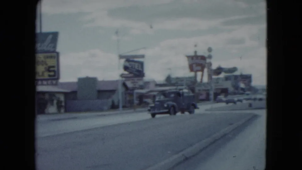 1959 Nevada home-movie frame looking down a road past vintage cars, low motel buildings, and roadside lodging signs.