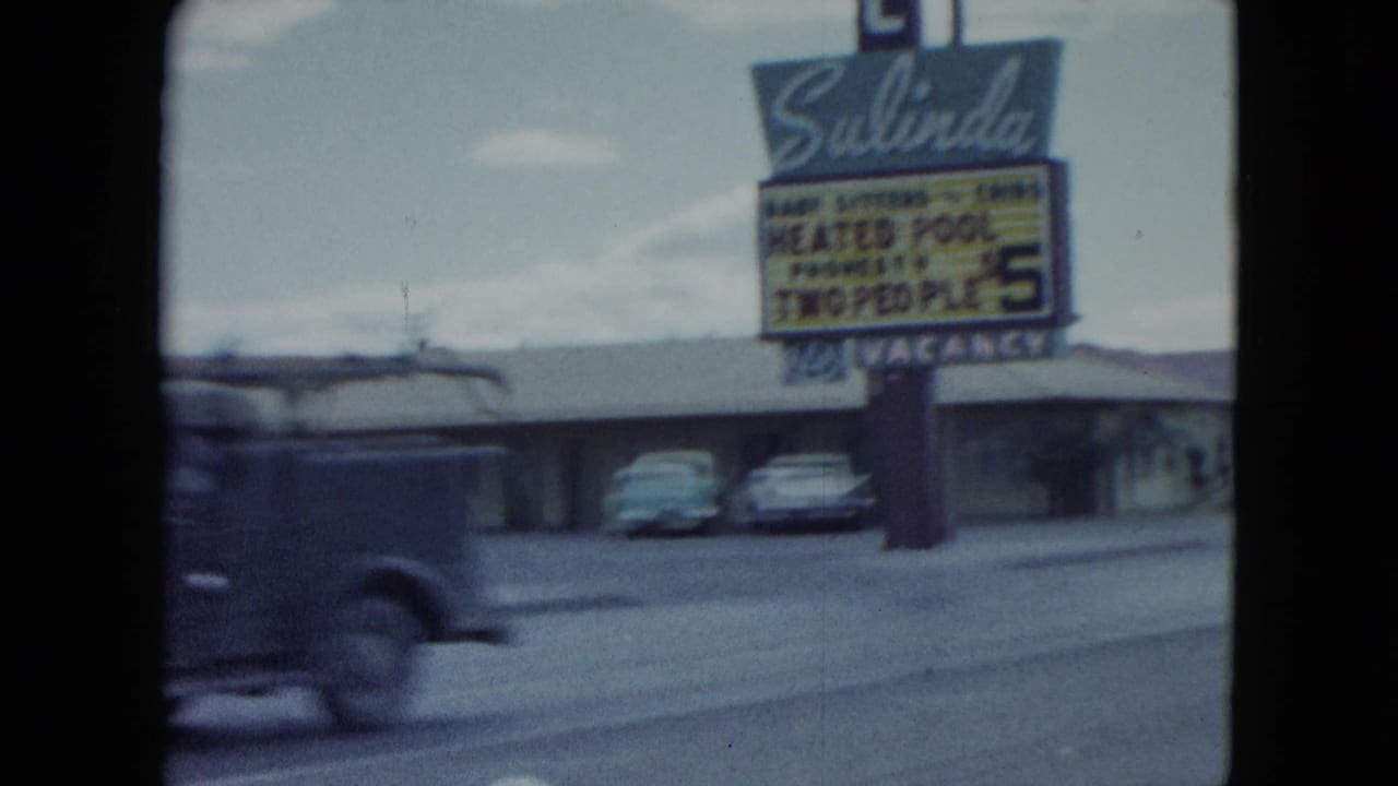 1959 Nevada home-movie frame with the Salinda Motel sign, heated pool wording, parked cars, and a passing vehicle blurred by motion.