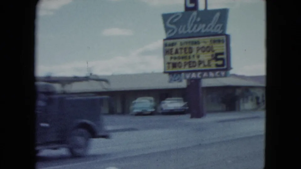 1959 Nevada home-movie frame with the Salinda Motel sign, heated pool wording, parked cars, and a passing vehicle blurred by motion.
