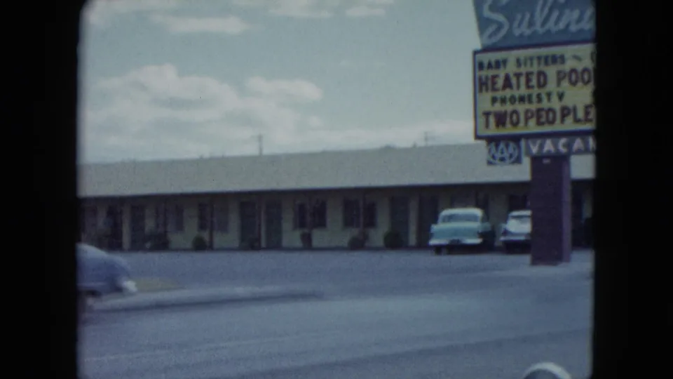 1959 Nevada frame showing a low motel building, parked cars, open roadside pavement, and the cropped Salinda Motel sign at right.