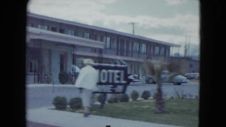 1959 Nevada home-movie frame showing a woman near a motel sign and low roadside lodging building.