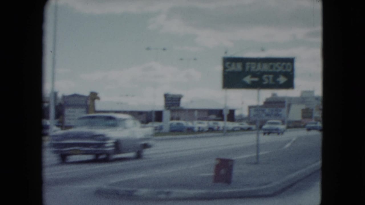 San Francisco St. directional sign beside a roadway with a passing car.