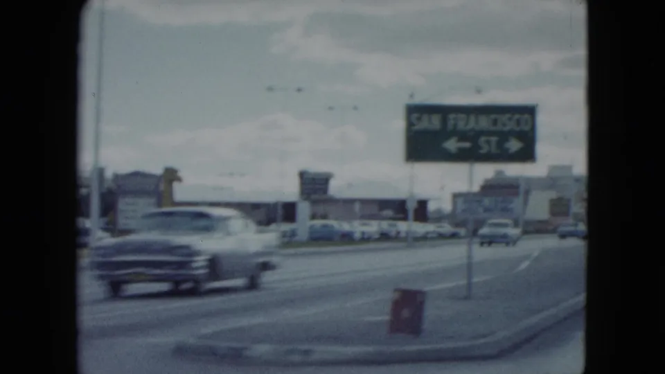 Directional San Francisco St. sign along a Nevada roadway as a late-1950s car passes in soft motion blur.