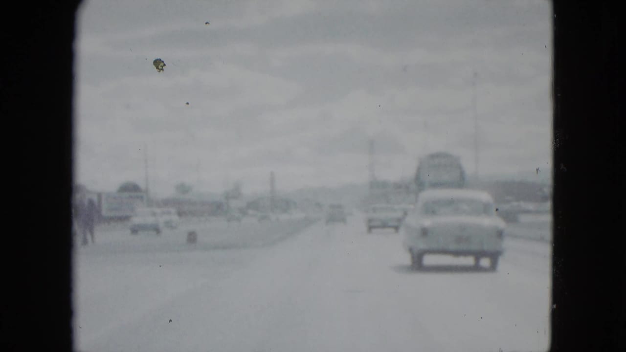 Cars travel ahead on a bright roadway with a rounded sedan in the right lane.