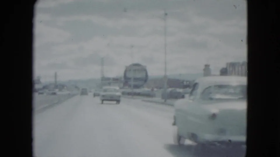 1959 Nevada roadway view with a bus-like vehicle ahead, light traffic, lane markings, utility poles, and a nearby car at the right edge.