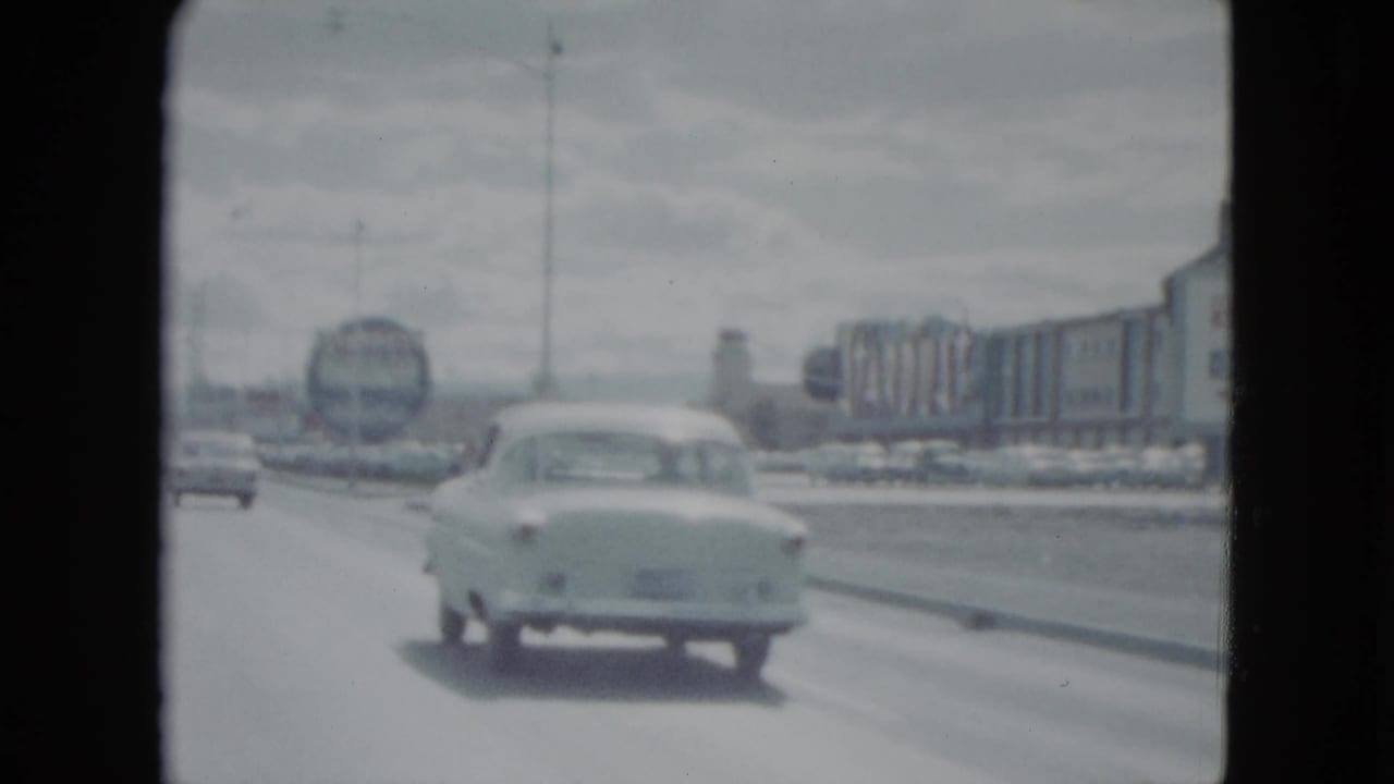 Car driving on a broad road past commercial buildings and roadside signs.