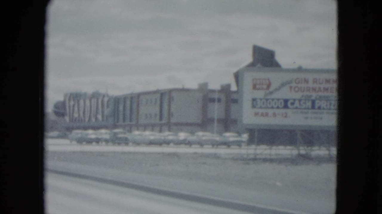 1959 Nevada 8mm frame showing a large cash-prize tournament sign beside roadside commercial architecture.