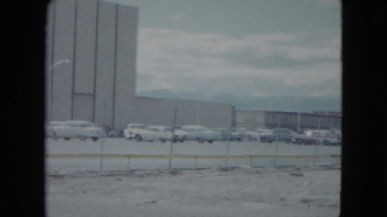 Tall building wall, parking lot, and cars under an overcast sky.