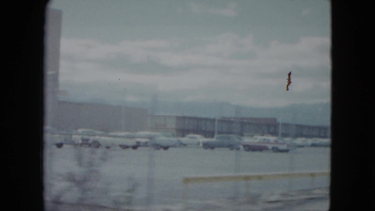Wide 1959 Nevada home-movie view across a parking area with rows of cars and low commercial buildings.