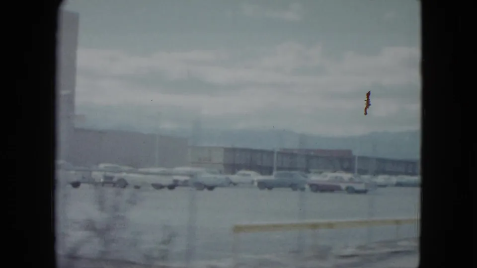 Wide 1959 Nevada home-movie view across a parking area with rows of cars and low commercial buildings.