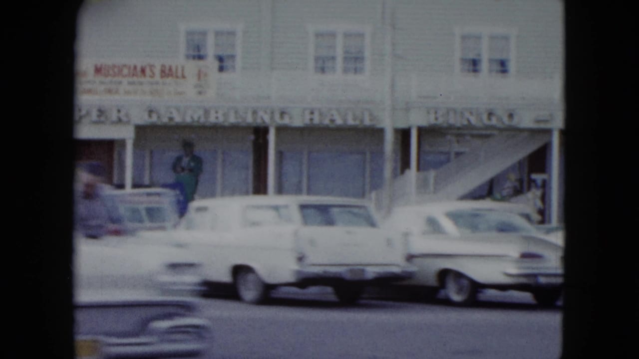 Cars pass and park in front of a gambling hall storefront.